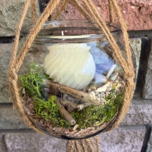 Pot suspendu artisanal en bois flotté avec mousse naturelle, poussière de bois et bougie décorative.