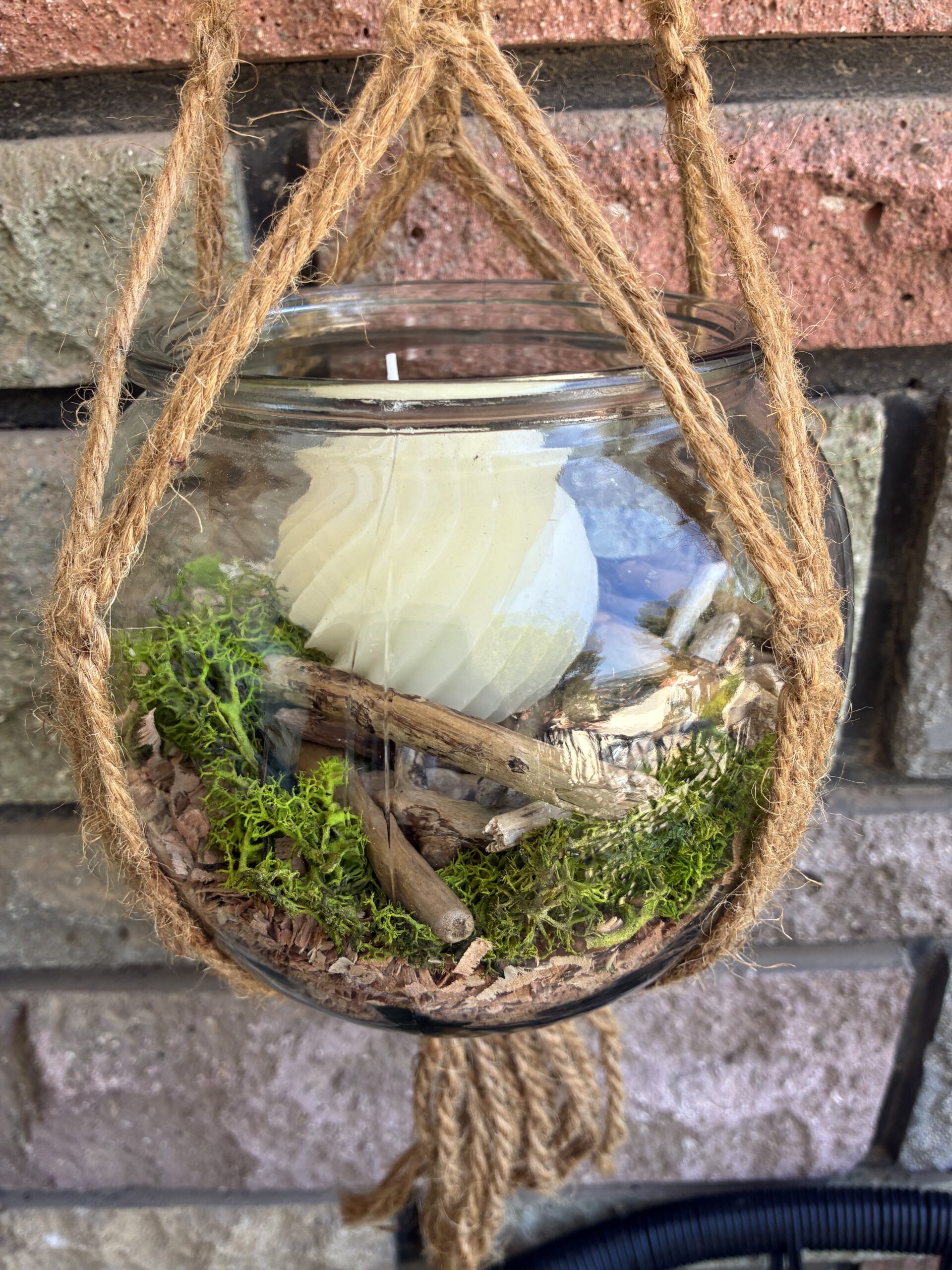Pot suspendu artisanal en bois flotté avec mousse naturelle, poussière de bois et bougie décorative.